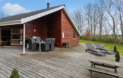 a wooden deck with chairs and a table and a building at Cozy Home In Spøttrup With Sauna in Spottrup