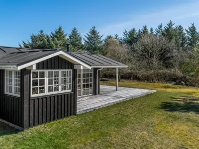 a large black shed with a deck in the grass at Holiday Home Jork - 1km from the sea by Interhome in Saltum