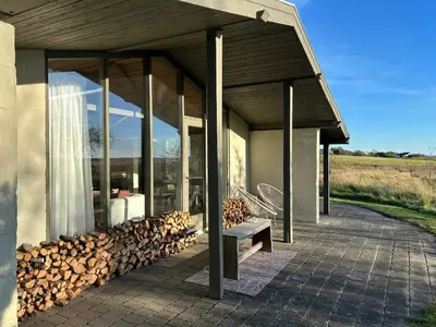 a building with a bench and a pile of fire wood at Summer House With Fields And Fjord Views in Thyholm