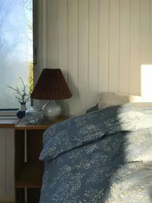 a bed with a blue blanket and a lamp on a table at Cozy Wagon House With Views Over The Limfjord in Roslev
