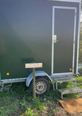 a sign in front of a green trailer with a door at Cozy Wagon House With Views Over The Limfjord in Roslev
