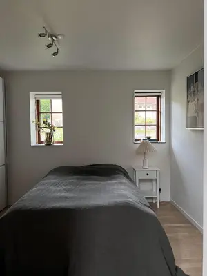 a white bedroom with a bed and two windows at Stalden ved Hjarbækgård in Løgstrup
