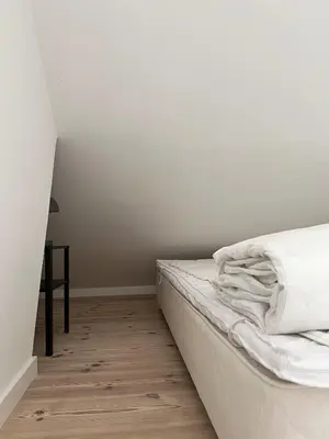 a bedroom with a bed with white sheets and a table at Stalden ved Hjarbækgård in Løgstrup