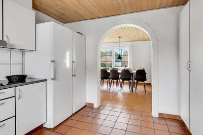 a kitchen with white cabinets and a table with black chairs at Large Pool House For 24 People, With Almost Everything In Activities, 300 Meters From The Fjord in Vinderup