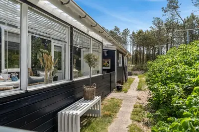 a black house with windows and a bench at Beautifully Renovated Holiday Home With Covered Terrace And Wood-Burning Stove, Close To The North Sea In Thy in Sønder Vorupør