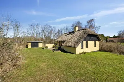 an old house with a thatched roof in a field at Astrup Vig Hideaway, Thatched Cottage with Shelter & Serenity in Roslev