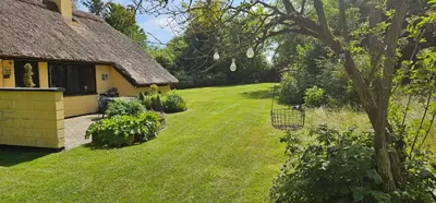 a backyard of a house with a grass yard at Astrup Vig Hideaway, Thatched Cottage with Shelter & Serenity in Roslev