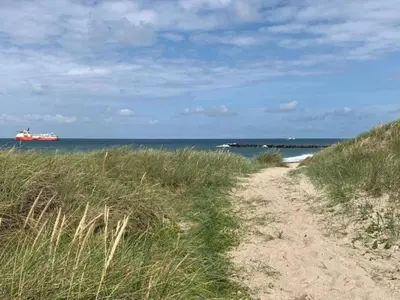 a dirt path to the beach with a ship in the water at 4 star holiday home in Thyborøn in Thyborøn