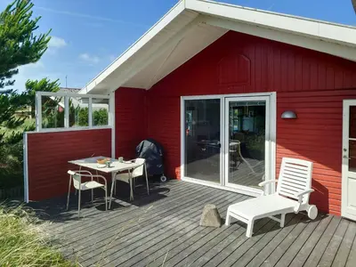 a red house with a table and chairs on a deck at Holiday Home Overlooking Protected Dune Heath in Frøstrup