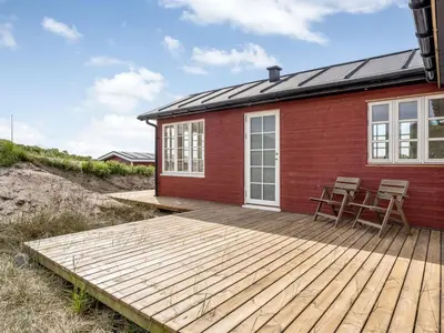 a red house with a deck and chairs on it at Holiday Home Thine - 250m from the sea by Interhome in Harboør