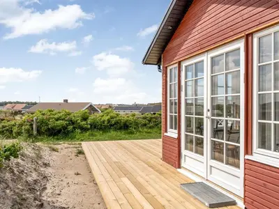 a wooden deck next to a red house at Holiday Home Thine - 250m from the sea by Interhome in Harboør