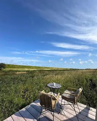 two chairs and a table on a boardwalk with a field at Agger Glamping - Lyngheden in Vestervig