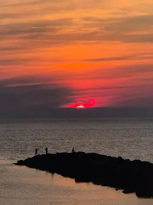 people standing on a pier in the ocean with a sunset at Ny lækker lejlighed på Havnen in Thyborøn