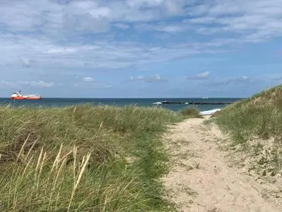 a dirt path to the beach with a ship in the water at 4 star holiday home in Thyborøn in Thyborøn