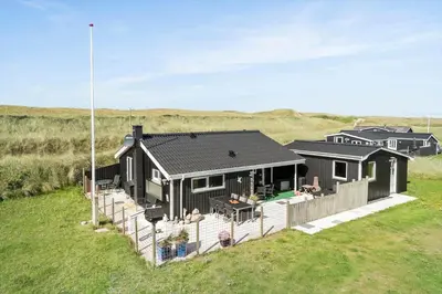 a black house with a wooden fence in a field at 306-Vestervig-Klitvej-6 in Vestervig