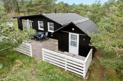 a black cabin with a table and a white fence at 645-Thisted-Blabaervej-4 in Thisted