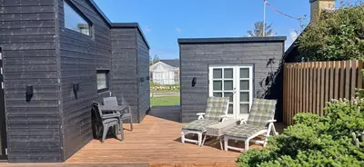 a small black house with chairs and a deck at Blokhus - tæt på by og strand in Blokhus