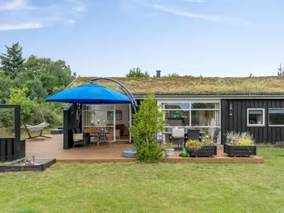 a house with a deck with a blue umbrella at Holiday Home Selvi - 2-2km from the sea by Interhome in Blokhus