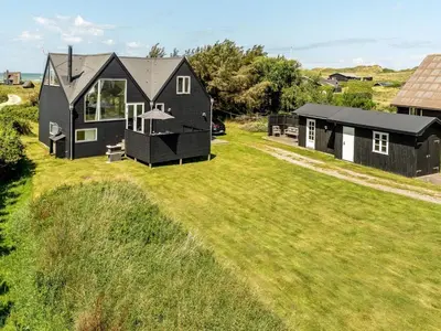 a black house on a grassy field with a building at Holiday Home Tekla - 180m from the sea by Interhome in Blokhus
