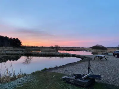 a picnic table next to a lake with a sunset at 4 person holiday home in Bøvlingbjerg in Bøvlingbjerg