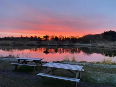 two picnic tables in front of a lake at sunset at 4 person holiday home in Bøvlingbjerg in Bøvlingbjerg
