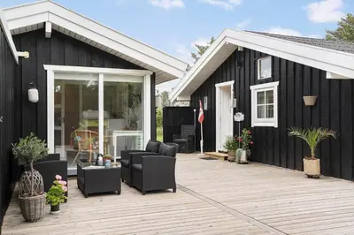 a black house with a wooden deck with chairs at LK2087-Lokken-Karinavej-54 in Løkken