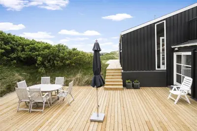 a black house with a table and an umbrella on a deck at LK157-Lokken-Ruthsvej-15 in Løkken