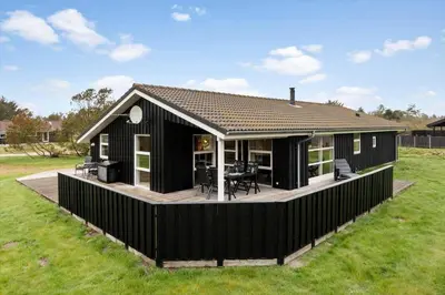 a black house with a deck in a field at LK1325-Lokken-Karinavej-59 in Løkken