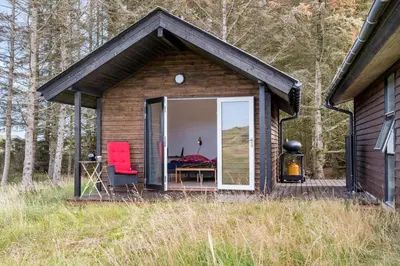 a small cabin with a red chair and a bedroom at LK2007-Lokken-Stellavej-11 in Løkken