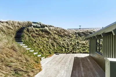 a house with a wooden walkway next to a hill at LK1985-Lokken-Monasvej-24 in Løkken