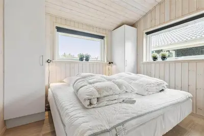 a bedroom with a bed with white sheets and two windows at LK902-Lokken-Mievej-42 in Løkken