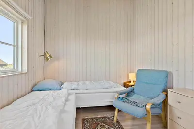 a small bedroom with a bed and a chair at LK528-Lokken-Rosavej-5 in Løkken