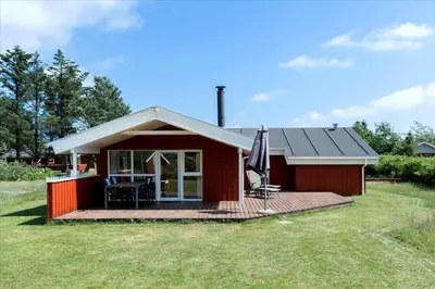 a red cottage with a deck and an umbrella at LK504-Lokken-Kristavej-23 in Løkken