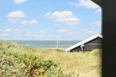 a house on the beach with the ocean and a flag at LK1947-Lokken-Madsinesvej-11 in Løkken