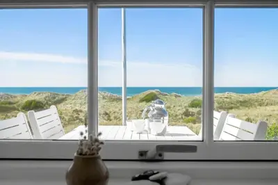 a table with white chairs in front of a window at LK1990-Lokken-Lottesvej-27 in Løkken