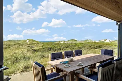 a wooden table with chairs and a view of the ocean at BL1679-Blokhus-Gormsvej-33 in Blokhus