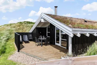 a black house with a grass roof and a wooden deck at BL416-Saltum-Revlingevej-28 in Saltum