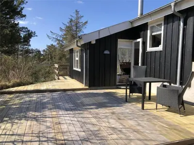 a black house with a table and chairs on a deck at BL547-Blokhus-Skraavejen-8 in Blokhus