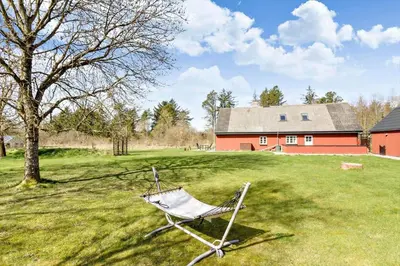 a chair sitting in a field in front of a red barn at BL1454-Pandrup-Rodhusvej-215 in Pandrup