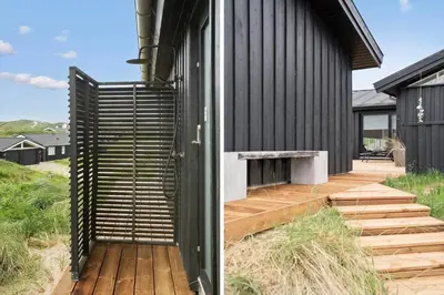 a black house with a wooden deck next to a building at BL1450-Blokhus-Klitvejen-99 in Blokhus