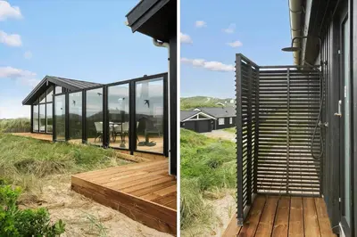 a house with glass walls and a wooden deck at BL1450-Blokhus-Klitvejen-99 in Blokhus