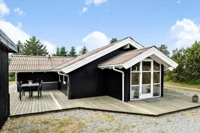 a black house with a deck and a table at BL1438-Blokhus-Bloksbjerg-82 in Blokhus