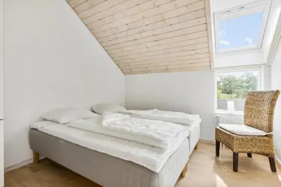 a bedroom with a bed and a chair and a window at BL1619-Blokhus-Klitheden-Nord-42 in Blokhus