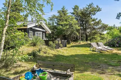 a house with two chairs and a bench in the yard at BL445-Blokhus-Bag-Hojen-65 in Blokhus