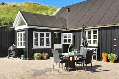 a black house with a table and chairs and an umbrella at BL1273-Blokhus-Vester-Klitvej-15 in Blokhus