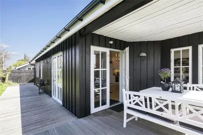a black house with a deck with a white table at BL475-Blokhus-Peder-Madsensvej-21 in Blokhus