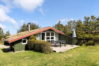 a green cottage with a table and an umbrella at BL794-Pandrup-Hunetorp-Klitvej-113 in Pandrup