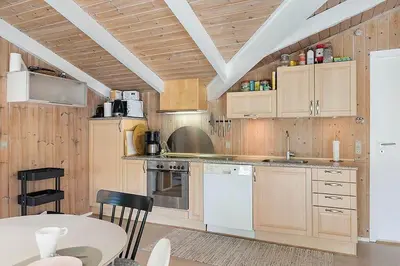 a kitchen with wooden cabinets and a table and a table and chairs at BL1052-Blokhus-Berberisvej-22 in Blokhus