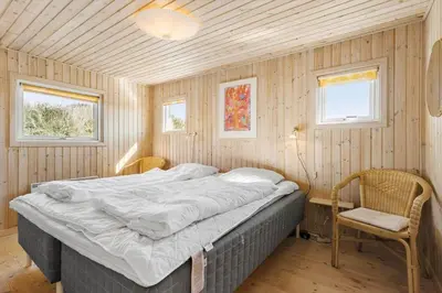 a bedroom with a bed and a chair and two windows at BL826-Saltum-Haresvinget-7 in Saltum