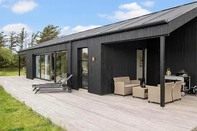 a black house with a wooden deck with a gym at BL1411-Blokhus-Ribergaardsvej-15 in Blokhus